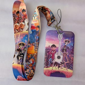 May include: A colorful lanyard and ID holder featuring characters and scenes from the animated movie "Coco." The lanyard and ID holder have a vibrant design with images of characters, guitars, and festive backgrounds. The ID holder has a metal clasp.