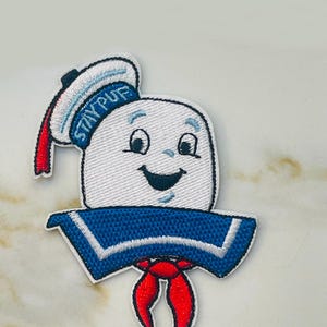 May include: Embroidered patch featuring a white marshmallow character with a blue sailor hat and red scarf. The hat has the text "STAY PUFF" on it.