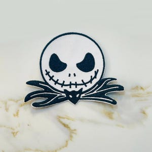 May include: Black and white embroidered iron-on patch featuring the face of Jack Skellington from the movie The Nightmare Before Christmas.