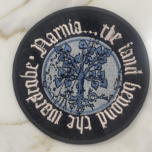 May include: A black and white embroidered patch with a tree in the center and the text "The Chronicles of Narnia, The Lion, The Witch and The Wardrobe" around the tree.