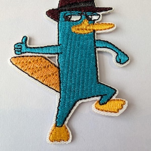 May include: Embroidered patch featuring a cartoon platypus character in teal, orange, and brown. The platypus is wearing a brown fedora and giving a thumbs-up. The patch has a white border and is likely for clothing or accessories.