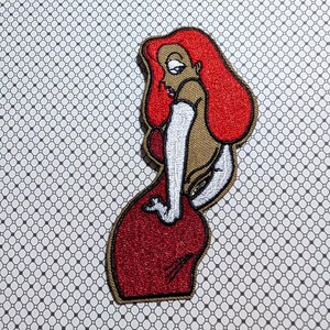 May include: Embroidered patch featuring a cartoon woman in a red dress and red hair. The patch has a gold border and white gloves. The woman is in a side profile pose, with a suggestive posture. The background is a white and gray pattern.