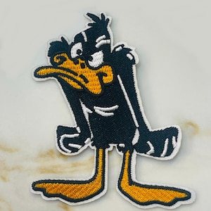 May include: Embroidered patch featuring Daffy Duck in a classic pose. The patch has a black body, yellow beak and feet, and white accents. The edges are outlined with white stitching.