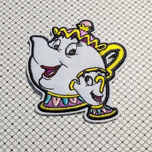 May include: Embroidered patch featuring a smiling teapot and teacup character with yellow, purple, and teal accents. The patch has a black border and is on a patterned background. The teapot has a yellow handle and crown.