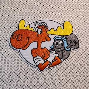 May include: Embroidered patch featuring cartoon characters Bullwinkle J. Moose and Rocky the Squirrel. Bullwinkle is orange with yellow antlers, white gloves, and a white circle background. Rocky is gray with a blue aviator cap. The patch is on a patterned background.