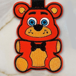 May include: Red and orange embroidered plush toy bear with a black bow tie and a black top hat. The bear has blue eyes and a black nose.
