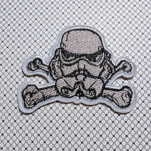 May include: Embroidered patch featuring a Stormtrooper helmet design over crossed bones. The patch is primarily gray with black detailing and a white border. The patch is on a patterned background.
