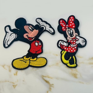 May include: Two embroidered iron-on patches featuring Mickey Mouse and Minnie Mouse. Mickey is wearing red shorts and yellow shoes. Minnie is wearing a red dress with white polka dots and a red bow with white polka dots.