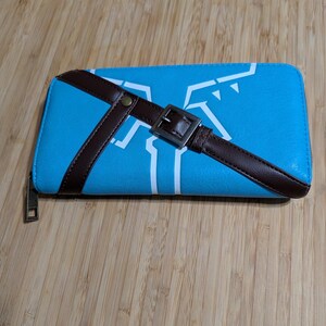 May include: A blue zippered wallet with a brown strap and buckle. The strap is designed to look like a belt. The wallet has a white graphic design on the front.