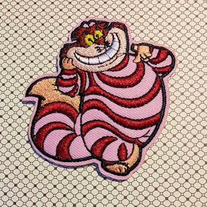 May include: Embroidered patch featuring the Cheshire Cat from Alice in Wonderland. The patch has a pink background with red stripes and a smiling face. The patch is outlined in pink and has a light brown tail.