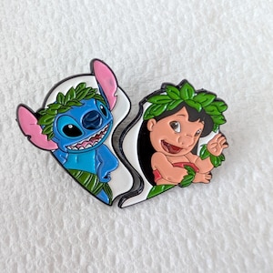 May include: A split heart-shaped enamel pin featuring the characters Stitch and Lilo from the animated film Lilo & Stitch. Stitch is blue with pink ears, and Lilo is wearing a red dress. Both characters are adorned with green leaf crowns.