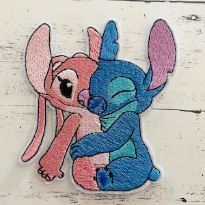 May include: Embroidered patch featuring Stitch and Angel from Lilo & Stitch. Stitch is blue with a light blue and green design, and Angel is pink with a white design. They are hugging each other.