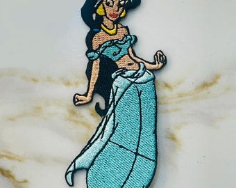 May include: An embroidered iron-on patch featuring a cartoon image of Princess Jasmine from Disney's Aladdin. She is wearing a blue outfit with a gold belt and a blue head scarf.