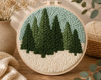 May include: A circular embroidery hoop containing a punch needle textile art piece. The design features a forest of dark green pine trees against a light sage green sky, with a textured white snowy ground at the base of the trees.