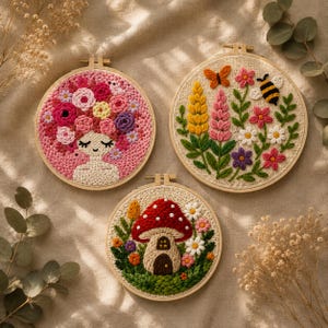 Op de afbeelding: Drie ronde borduurringen met gestructureerd handwerk. Eén toont een figuur met een bloemrijk kapsel, een andere een tuin met een vlinder en bij, en de derde een paddenstoelhuis omringd door kleine bloemen en groen bladwerk.