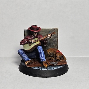 May include: A miniature figurine of a man wearing a red shirt, blue jeans, and a brown cowboy hat, playing a guitar while sitting next to a brown dog. The figurine is on a black base with a brown and gray textured surface.