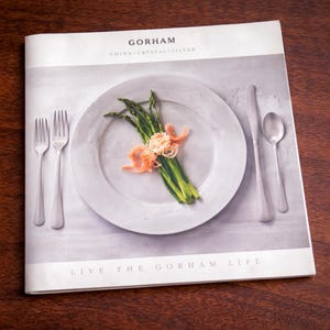 May include: A magazine spread featuring Gorham China, Crystal, and Silver. A white plate holds asparagus and garnishes, with silverware arranged around it. The text "LIVE THE GORHAM LIFE" is visible at the bottom of the page.