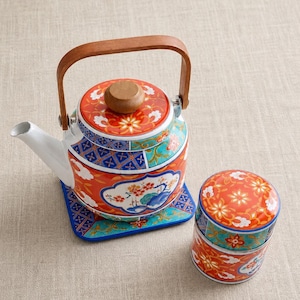 May include: A decorative ceramic teapot and matching container set. The teapot has a wooden handle and lid, and the set features a vibrant floral and geometric pattern in red, blue, and white. The teapot sits on a square coaster.