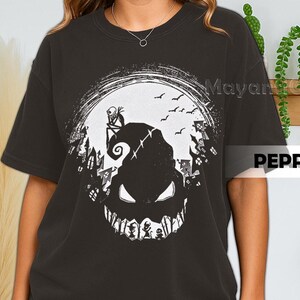 K&ouml;nnte beinhalten: Dunkelgraues T-Shirt mit einem wei&szlig;en Aufdruck eines gruseligen Charakters mit breitem Grinsen, vor einem Vollmond mit Flederm&auml;usen und einer Stadtsilhouette. Das Shirt hat die Texte "Mayan" und "PEPPI".
