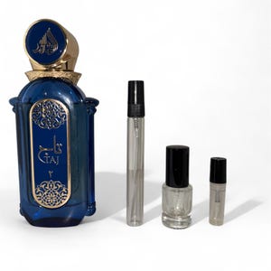 May include: A dark blue perfume bottle with gold accents and the word "TAJ" in gold lettering. The bottle is flanked by three smaller, clear bottles with black caps, likely for perfume samples or travel sizes.