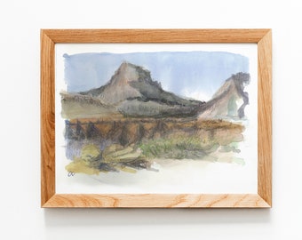 May include: A framed watercolor painting of a mountain landscape. The painting features two mountains in the distance, with a field of grass and trees in the foreground. The sky is a light blue color, and the mountains are a dark gray color.