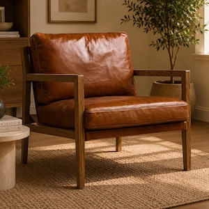 Puede incluir: Un sillón de cuero marrón con estructura de madera. La silla tiene forma cuadrada con asiento y respaldo acolchados. El marco de madera es de color marrón claro. La silla está colocada sobre una alfombra de yute tejida.