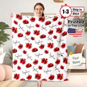 May include: White fleece blanket with a red poppy floral pattern and the name "Sophia" repeated throughout. The blanket is personalized with the option to add a name.