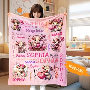 May include: Pink fleece blanket with a white cow and heart design. The blanket features the name "Sophia" repeated throughout the design.