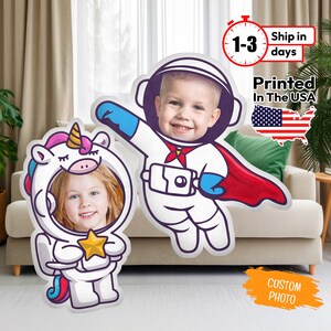 May include: Two photo booth cutouts, one of a unicorn astronaut holding a star and the other of an astronaut with a red cape. Both cutouts have spaces for a photo to be inserted.
