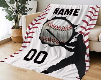 Puede incluir: Manta blanca con temática de béisbol con una pelota de béisbol rompiendo una pared, un bate de béisbol y la silueta de un jugador de béisbol. La manta tiene la palabra "NAME" y el número "00" impresos.