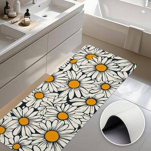 May include: A white and black bathroom rug with a daisy pattern. The daisies have yellow centers and white petals. The rug has a non-slip backing.