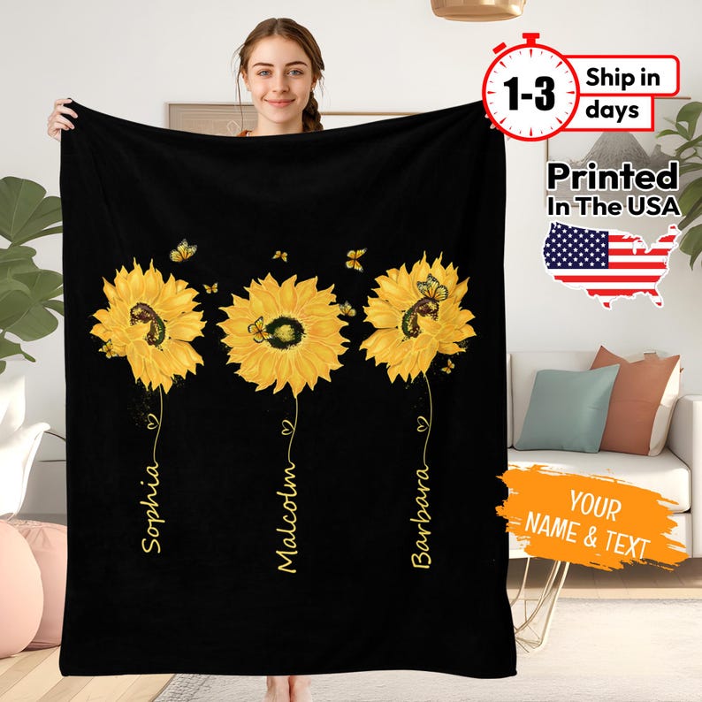 May include: Black fleece blanket featuring three yellow sunflowers with butterflies. Each sunflower has a name underneath: Sophia, Malcolm, and Barbara.