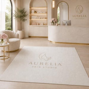 May include: A rectangular area rug featuring a light beige surface with the Aurelia Skin Studio logo printed in the center. The logo consists of a stylized profile outline and a leaf icon above the text Aurelia Skin Studio in a serif font.