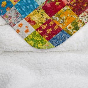 May include: A patchwork quilt with a variety of floral and geometric patterns in bright colors. The quilt is folded over a white fluffy blanket.