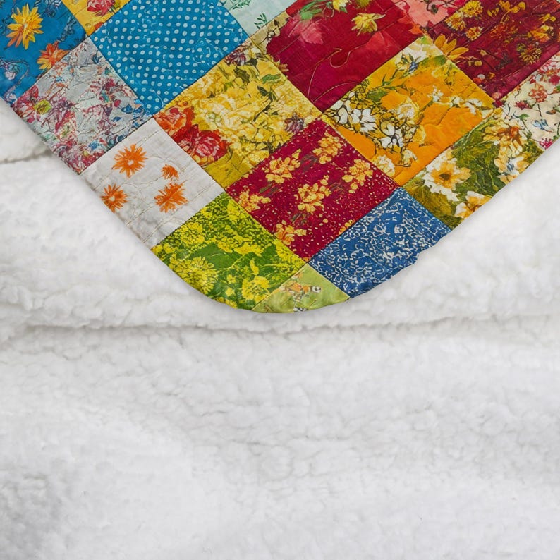 May include: A patchwork quilt with a variety of floral and geometric patterns in bright colors. The quilt is folded over a white fluffy blanket.
