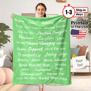 May include: Green fleece throw blanket with white text that reads "Warm, Calm, Healing, Vibes, Hugs, Well Wishes, Healing Energy, Zest For Life, Positive Thoughts, Persevere, Laughter, Love, Strong, You're Amazing, Comfort, Peace, Support, Here For You, Tranquility, Loving Hugs, Bravery, Much, You're Admired, Heroic, Peaceful Hope, Serenity, Spirit, Courageous, Prayer, Encouragement, Courage, Fun, Finish The Fight, Loving Hugs, Peace".