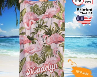 May include: A pink beach towel featuring a flamingo and tropical leaf pattern. The towel has the name "Madelyn" printed on it. The background shows a beach scene with blue water and sky.