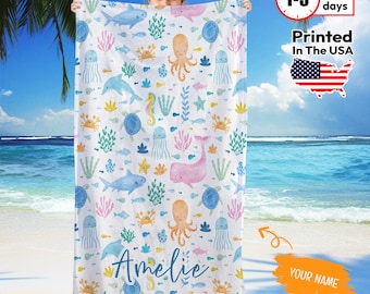 May include: White beach towel featuring a colorful sea life pattern with whales, octopuses, and jellyfish. The towel has the name "Amelie" in cursive script. Printed in the USA.