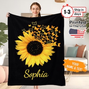 May include: Black fleece blanket featuring a yellow sunflower with a scattering of yellow butterflies. The name "Sophia" is printed in yellow at the bottom of the blanket.