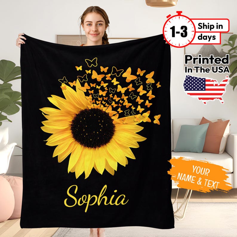May include: Black fleece blanket featuring a yellow sunflower with a scattering of yellow butterflies. The name "Sophia" is printed in yellow at the bottom of the blanket.