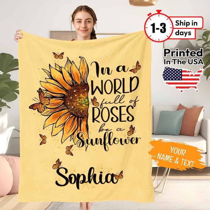May include: A yellow fleece blanket featuring a sunflower graphic and the text "In a world full of roses be a sunflower". The name "Sophia" is printed below the graphic.