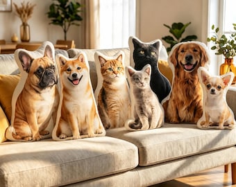 May include: A collection of six decorative throw pillows shaped like animals, including a French Bulldog, a Shiba Inu, a tabby cat, a grey cat, a black cat, and a Golden Retriever, arranged in a row on a light-colored fabric sofa.