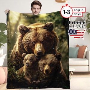 May include: A brown blanket featuring a detailed illustration of a bear family in a forest setting. The image shows a large bear with two cubs, with the text "Printed In The USA" and a US flag.