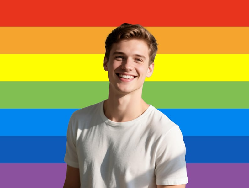 May include: A person wearing a white t-shirt smiles in front of a rainbow flag. The flag features horizontal stripes of red, orange, yellow, green, blue, and purple. The person has short brown hair.