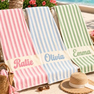 May include: Three rectangular beach towels featuring vertical stripes in pink, light blue, and sage green. Each towel has a solid white horizontal band at the bottom with a name embroidered in a matching color: Ratie in pink, Olivia in blue, and Emma in green.