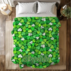 May include: A green blanket with a pattern of shamrocks and white flowers. The blanket has a scalloped edge and the name "Sophia" in a decorative font. The shamrocks are in various shades of green and patterns.