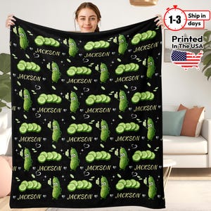 May include: Black blanket featuring a repeating pattern of cartoon pickles, cucumber slices, and the name "JACKSON". The pickles are green with smiling faces and thumbs up. White hearts and small white dots complete the design.