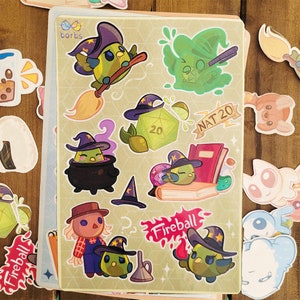 May include: A sticker sheet with cartoon bird wizard designs. The stickers show birds wearing witch hats, a cauldron, a d20 die, and the word "Fireball". The background is a light green colour with a diamond pattern.