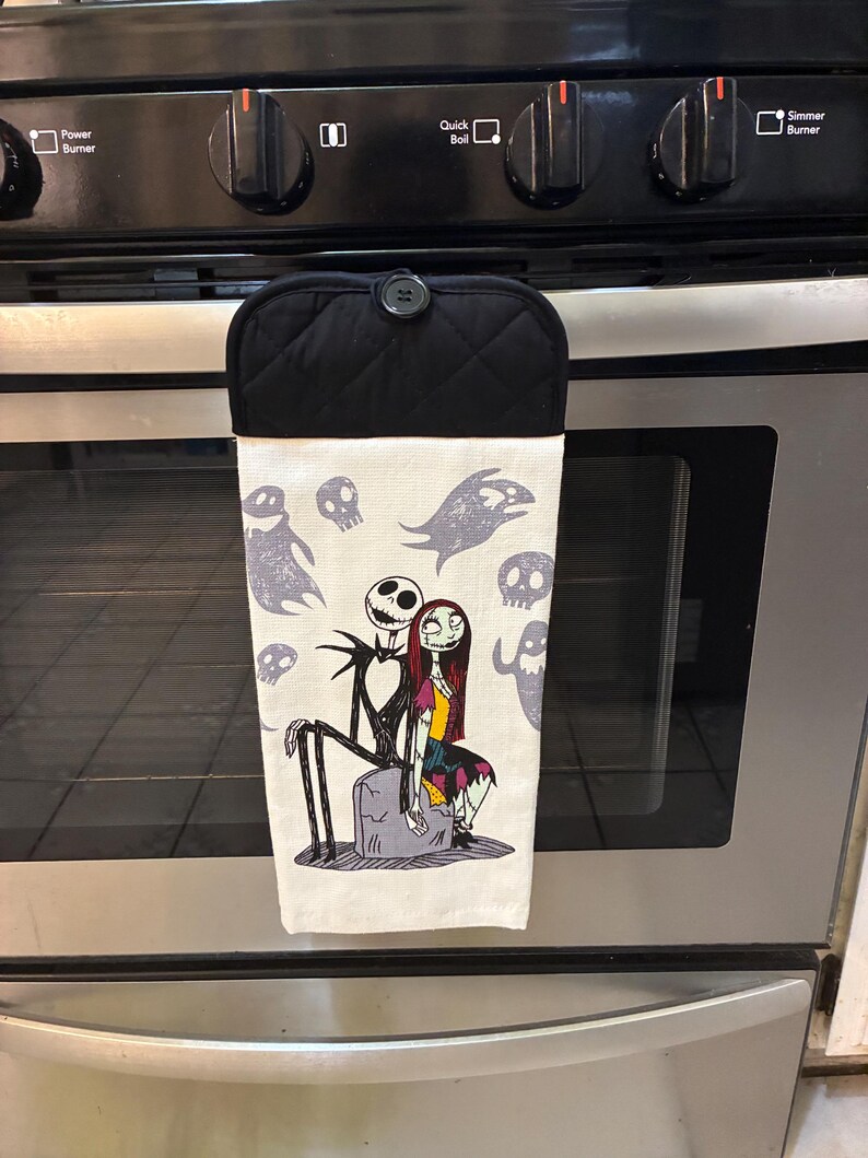 Puede incluir: Un pa&ntilde;o de cocina blanco con Jack Skellington y Sally de Pesadilla antes de Navidad, con dise&ntilde;os de fantasmas y calaveras grises. La parte superior es negra con un patr&oacute;n acolchado y un bot&oacute;n para colgar.