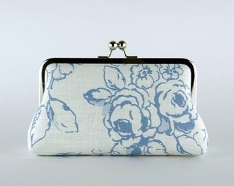 Könnte beinhalten: Eine weiße Clutch mit einem blauen Blumenmuster und einem silbernen Verschluss.
